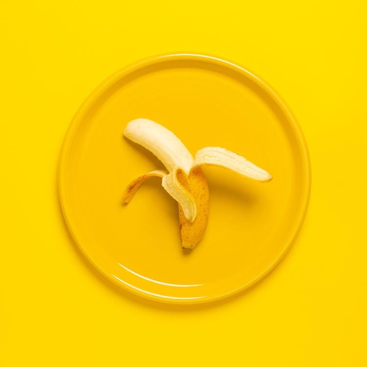 бесплатная Фотография очищенного банана на желтой тарелке и фоне Стоковое фото